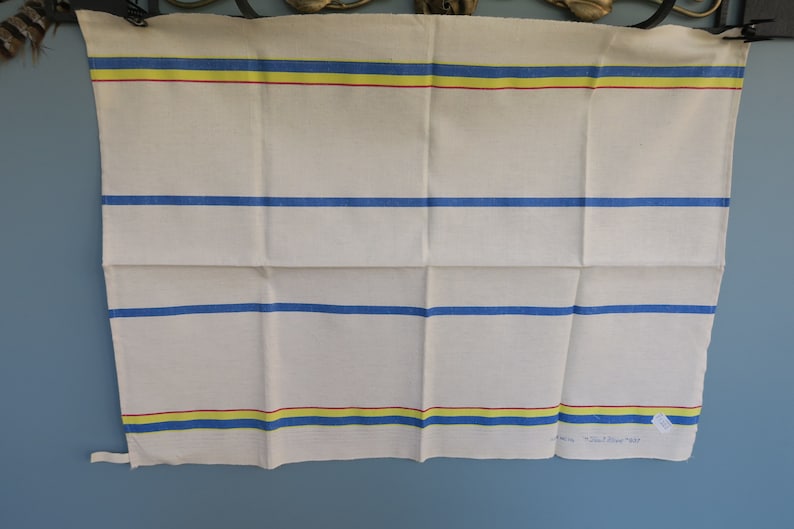 Puede incluir: Toalla de cocina blanca con rayas azules, amarillas y rojas. La toalla tiene un borde doblado y una peque&ntilde;a etiqueta que dice "Old River 1937".