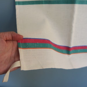 Puede incluir: Una toalla de cocina blanca con rayas verdes, rojas y azules. La toalla tiene un lazo para colgar.