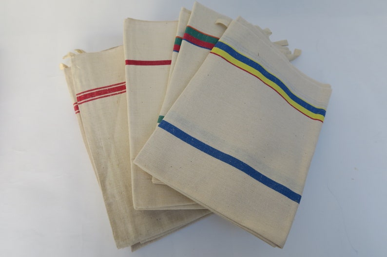 Puede incluir: Conjunto de cinco toallas de t&eacute; de algod&oacute;n blanco con rayas de colores. Las toallas tienen rayas rojas, azules, amarillas y verdes.