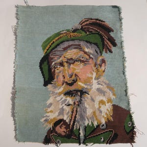 May include: Needlepoint portrait of an elderly man with a long white beard, wearing a green hat with a feather and a brown jacket. The background is a light blue color. The edges of the needlepoint are frayed.