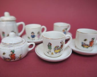 May include: A white porcelain tea set with a whimsical design featuring children and a wagon. The set includes a teapot, sugar bowl, creamer, and four teacups and saucers.