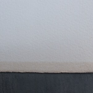 Pode incluir: Close-up da borda de uma folha de papel branca com uma superf&iacute;cie ligeiramente texturizada. O papel est&aacute; ligeiramente descolorido ao longo da borda.