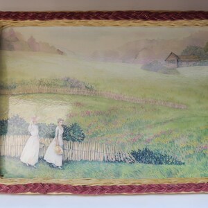 Op de afbeelding: Rechthoekig dienblad met een geweven rand in natuurlijke en bordeaux tinten. De lade heeft een pastorale scène met twee figuren in witte jurken die in een veld lopen. De scène omvat een houten hek, een huis en een groen landschap.
