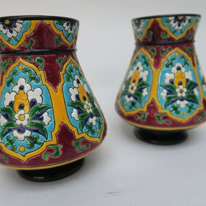May include: Two decorative ceramic vases with a floral pattern in shades of red, blue, green, yellow, and white. The vases have a black base and a flared shape.