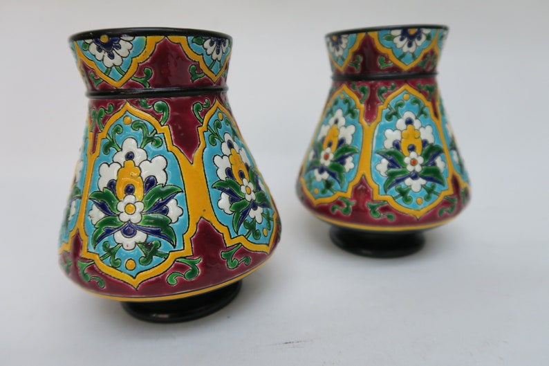 May include: Two decorative ceramic vases with a floral pattern in shades of red, blue, green, yellow, and white. The vases have a black base and a flared shape.