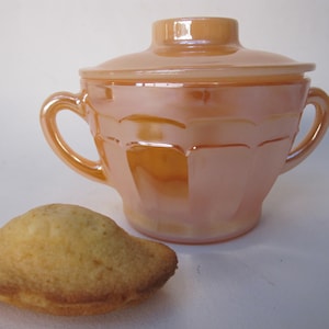 Peut inclure: Un sucrier en verre pêche avec un couvercle et deux anses. Le bol présente un motif géométrique et se trouve à côté d'un biscuit madeleine brun doré. Un article de cuisine classique.