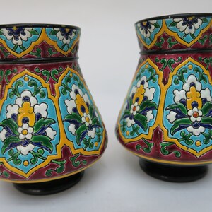 May include: Two decorative ceramic vases with a colorful floral pattern. The vases are a dark red color with blue, green, yellow, and white floral designs.