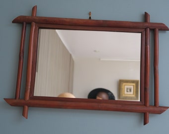 May include: A rectangular mirror with a dark wood frame. The frame is made of multiple pieces of wood that are joined together in a unique design. The mirror is hanging on a light blue wall.