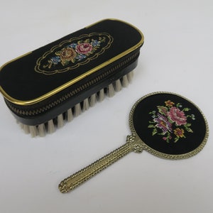 May include: A vintage black brush and mirror set with floral embroidery. The brush is in a black case with a gold trim and zipper. The mirror has a silver handle and a black frame with floral embroidery.