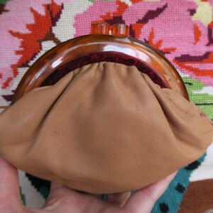 May include: A brown leather purse with a tortoise shell frame and a red velvet lining. The purse is closed and has a gathered top.