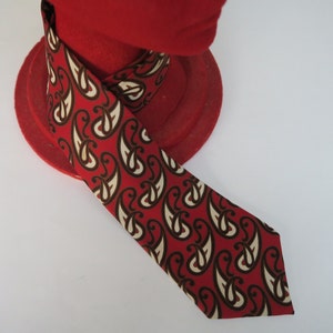 May include: A red tie with a paisley pattern in white and brown. The tie is on a red hat stand.