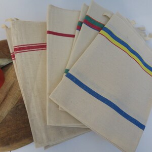 Puede incluir: Conjunto de cinco toallas de cocina blancas con rayas de colores. Las toallas tienen rayas rojas, azules, amarillas y verdes.