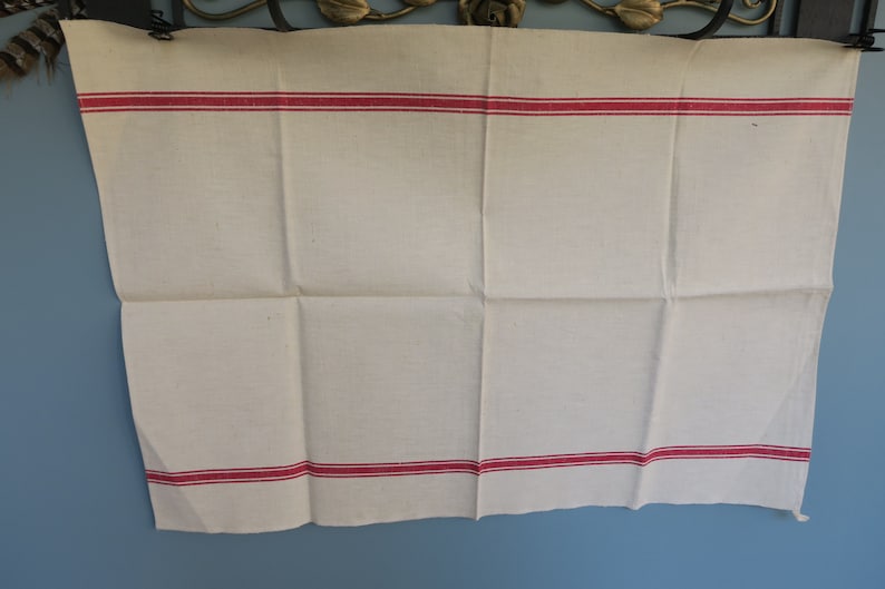 Puede incluir: Un pa&ntilde;o de cocina de lino blanco con dos rayas rojas en los bordes superior e inferior.