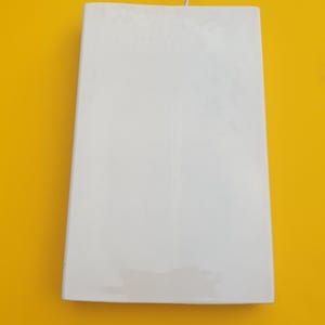 May include: A white rectangular object with a slight trapezoid shape, possibly a light fixture or decorative panel. The object is against a bright yellow background, with a thin white wire extending from the top.