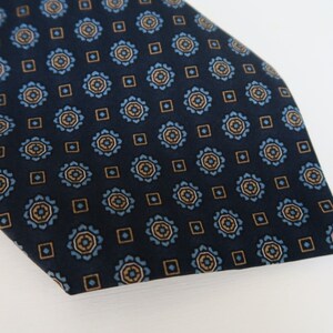 May include: A dark blue tie with a repeating pattern of small blue and gold circles and squares.