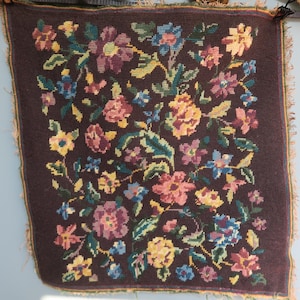 Puede incluir: Textil cuadrado de punto de aguja marrón oscuro con un patrón floral. El diseño presenta varias flores en tonos de rosa, amarillo, azul y morado, con hojas verdes. Los bordes tienen un borde deshilachado de color beige.