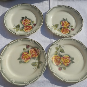 May include: Four white ceramic plates with a decorative floral design featuring yellow and orange roses. The plates have a scalloped edge and a green and white border.