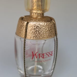 Puede incluir: Un frasco de perfume Yvresse de Yves Saint Laurent de vidrio transparente. El frasco tiene una tapa dorada y una banda dorada alrededor del medio. El frasco está etiquetado con "Yvresse Eau de Toilette".
