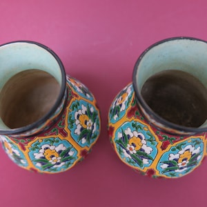 May include: Two ceramic vases with a colorful floral pattern. The vases are decorated with blue, green, yellow, red, and white flowers. The vases are empty and have a light blue glaze on the inside.