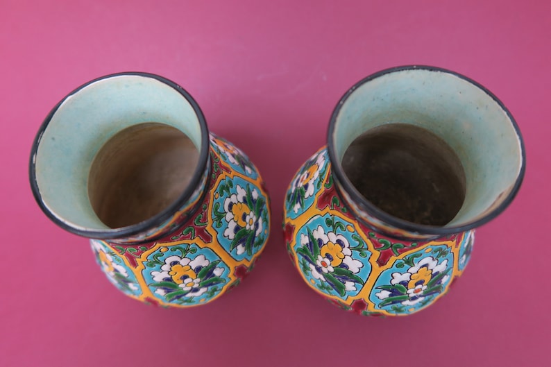 May include: Two ceramic vases with a colorful floral pattern. The vases are decorated with blue, green, yellow, red, and white flowers. The vases are empty and have a light blue glaze on the inside.