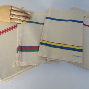 Puede incluir: Conjunto de cinco toallas de cocina vintage con rayas de colores. Las toallas son de algod&oacute;n blanco y tienen rayas rojas, azules, amarillas y verdes. Una toalla tiene el texto "TOILE METIS" impreso.