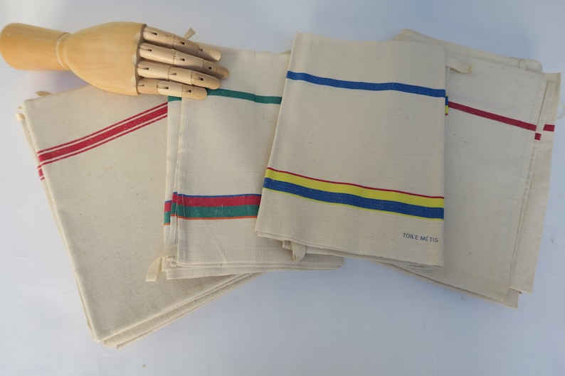 Puede incluir: Conjunto de cinco toallas de cocina vintage con rayas de colores. Las toallas son de algod&oacute;n blanco y tienen rayas rojas, azules, amarillas y verdes. Una toalla tiene el texto "TOILE METIS" impreso.