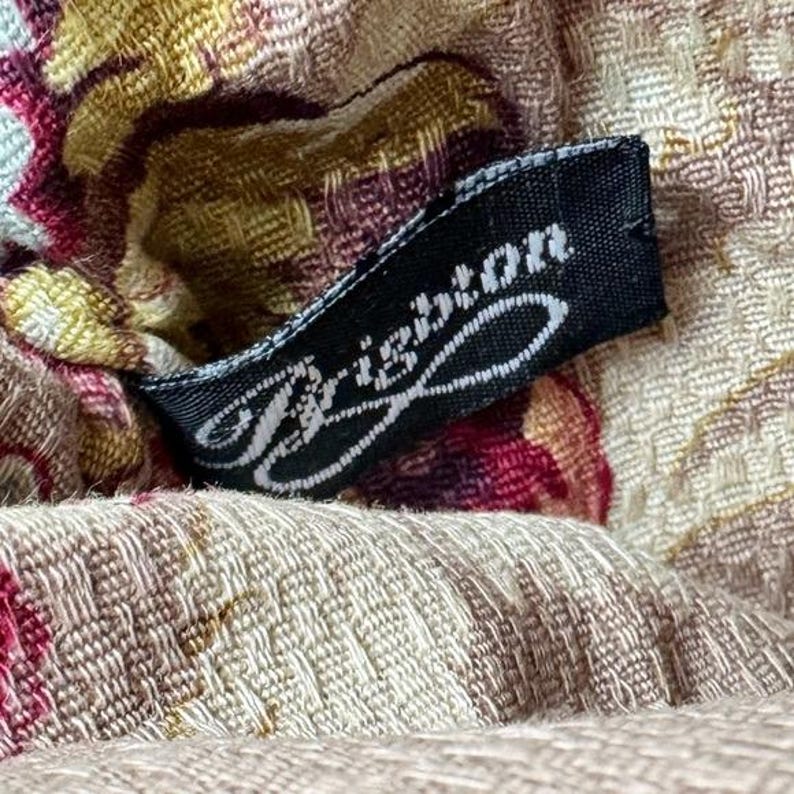 Może przedstawiać: Zbliżenie tkaniny z kwiatowym wzorem w odcieniach beżu, bordowego i ż&oacute;łtego. Czarna metka z napisem "Brighton" w białym skrypcie jest przymocowana do tkaniny.