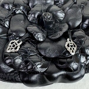 Może przedstawiać: Zbliżenie czarnej sk&oacute;rzanej torebki z kwiatowym wzorem. Torba ma teksturowany, wytłoczony wz&oacute;r i jest ozdobiona srebrnymi zawieszkami. Projekt zawiera r&oacute;żę i kształty przypominające płatki.