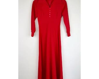 Può includere: Un lungo vestito rosso con colletto e chiusura con bottoni. Il vestito ha maniche lunghe e una gonna fluida.