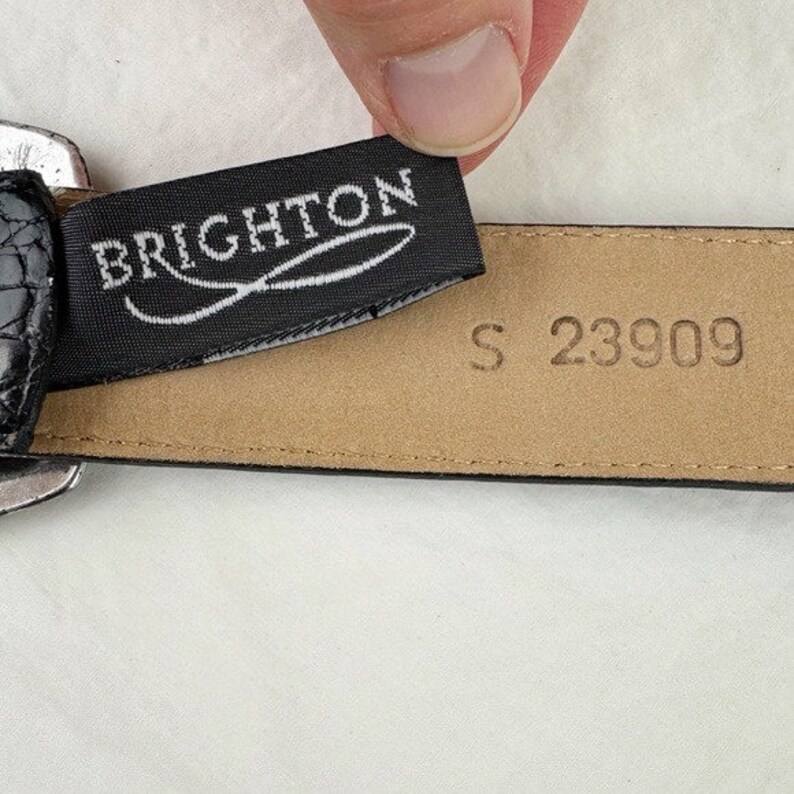 May include: Black leather belt with a silver buckle and a black fabric label that reads "BRIGHTON". The back of the belt has the size "S" and the number "23909" embossed on it.