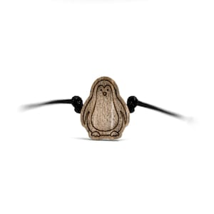 May include: A wooden penguin charm on a black cord bracelet.