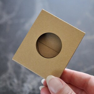May include: A brown cardboard box with a round hole cut out of the center. The box is held in a hand.