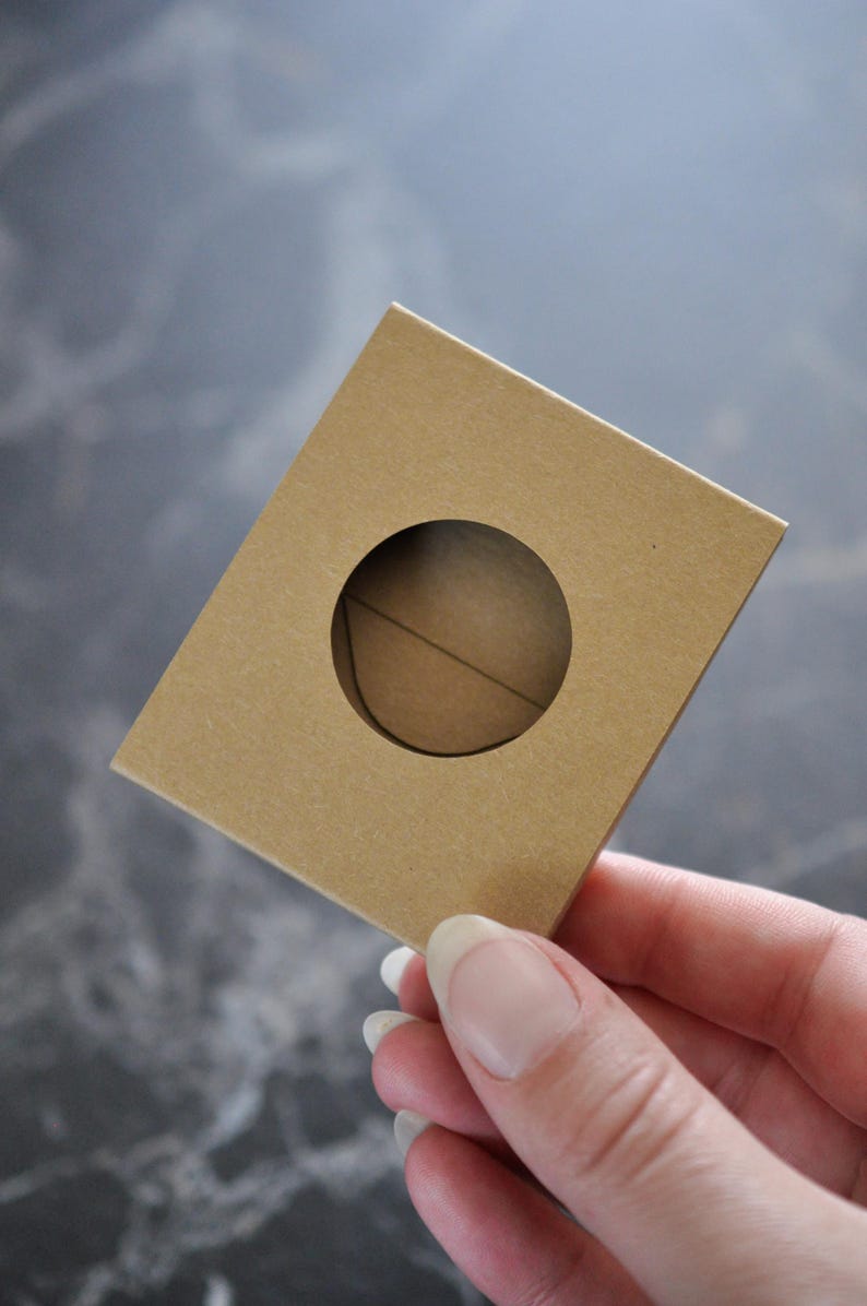 May include: A brown cardboard box with a round hole cut out of the center. The box is held in a hand.