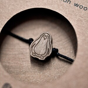 May include: A wooden penguin charm on a black string bracelet. The charm is made from Slovenian wood.