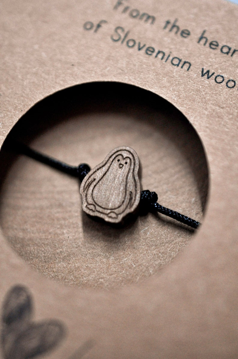 May include: A wooden penguin charm on a black string bracelet. The charm is made from Slovenian wood.