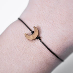 May include: A simple black cord bracelet with a wooden crescent moon charm.