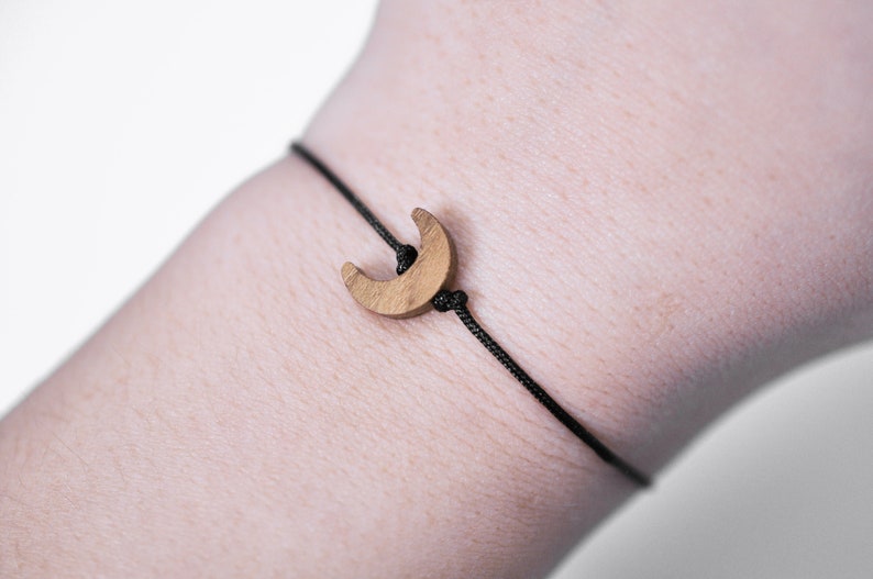 May include: A simple black cord bracelet with a wooden crescent moon charm.