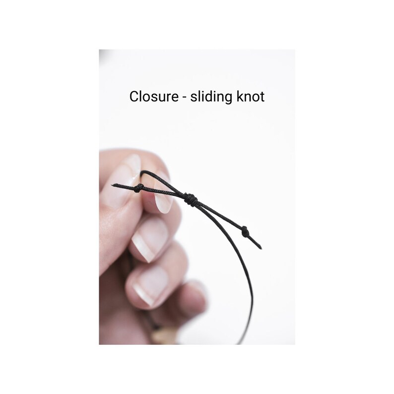 May include: A close-up of a black cord with a sliding knot closure. The cord is held in a hand, showing how the knot can be adjusted to fit.