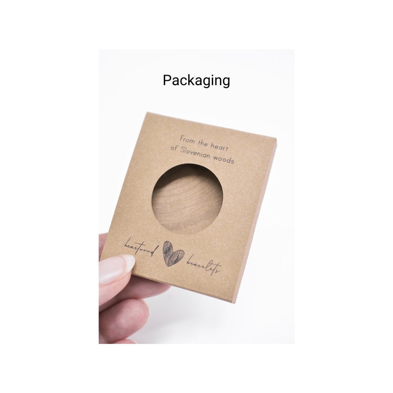 May include: A brown cardboard box with a cut-out window, showcasing a wooden bracelet. The box has the text "From the heart of Slovenian woods" and "heartwood bracelets" printed on it.