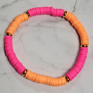 Puede incluir: Una pulsera vibrante con secciones alternas de cuentas de disco de color rosa brillante y melocotón. Cuentas de metal dorado separan las secciones de color. Un accesorio elegante.