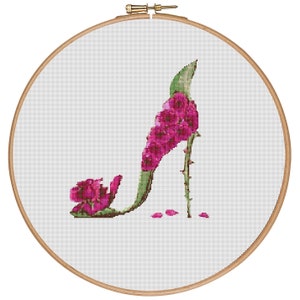 May include: A pink floral high heel shoe with a green stem and leaves. The shoe is in a wooden embroidery hoop.