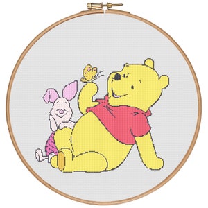 Pode incluir: Um aro de bordado de ponto cruz com um desenho de Winnie the Pooh e Porquinho. Winnie the Pooh é amarelo e usa uma camisa vermelha. Porquinho é rosa e tem um laço vermelho. Uma borboleta amarela voa perto de Winnie the Pooh.
