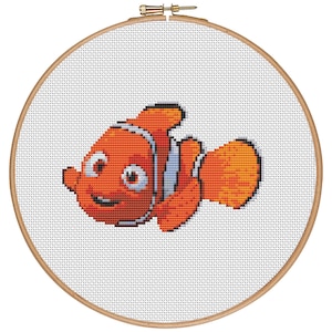 Può includere: Un primo piano di un ricamo a punto croce di un pesce pagliaccio arancione e bianco, noto anche come pesce anemoni, su uno sfondo bianco.