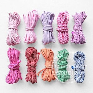 May include: A collection of ten bundles of colorful rope in various shades of pink, purple, red, orange, green, and blue. Each bundle is tightly wound and tied, showcasing a variety of patterns and textures.