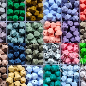 Puede incluir: Una colección de 12 colores diferentes de cuentas de dentición de silicona en forma geométrica. Las cuentas están dispuestas en una cuadrícula en un recipiente de plástico transparente.