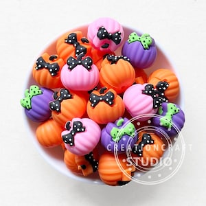 May include: A bowl filled with colorful Halloween-themed pumpkin charms. The charms are made of silicone and feature black polka dots, black bows, and green accents.
