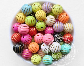 Puede incluir: Una colección de cuentas redondas y coloridas con un diseño acanalado y detalles dorados. Las cuentas son de varios colores, incluyendo rosa, naranja, amarillo, verde y azul, y están dispuestas en un cuenco blanco. Ideales para la creación de joyas.