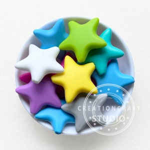 May include: A bowl filled with colorful star-shaped silicone beads. The beads are in various colors, including blue, green, yellow, purple, pink, and white.