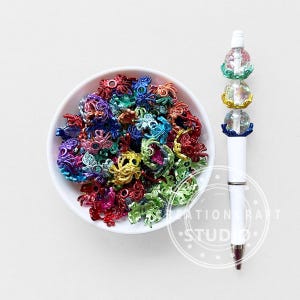 Peut inclure: Un stylo blanc avec un dessus décoratif orné de trois orbes en cristal avec des accents de filigrane colorés. Un bol blanc est rempli d'un assortiment de breloques pieuvres en filigrane colorées de différentes couleurs comme le rouge, le bleu et le vert.