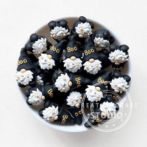 Op de afbeelding: Een kom gevuld met zwarte en witte gnomenvormige siliconen bedels met het woord "Boo" in goud op elke bedel.